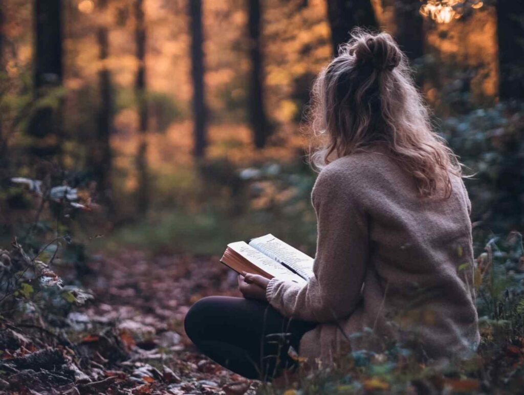 a women sitting on the forest floor, absorbed in reading a book. She dressed in a cozy beige sweater